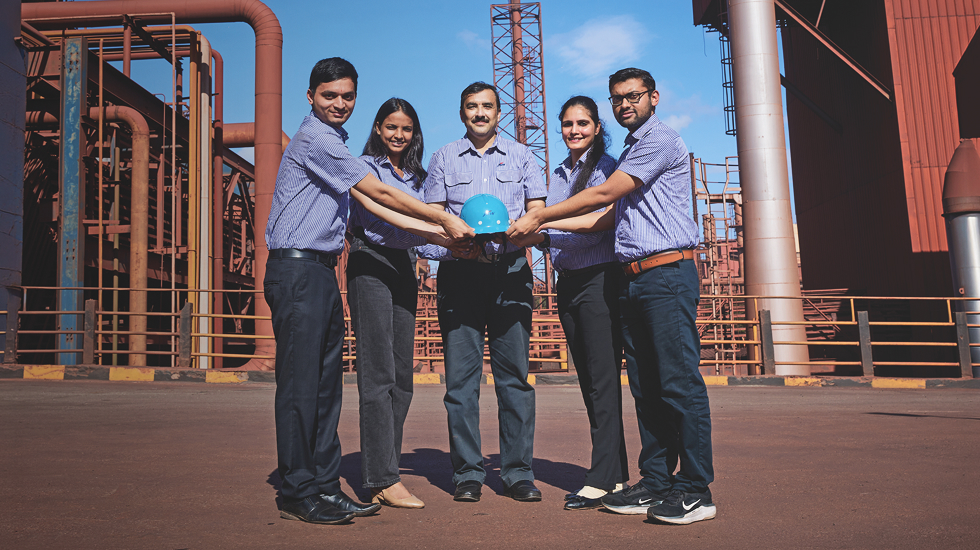 JSW Steel team holding a safety helmet together